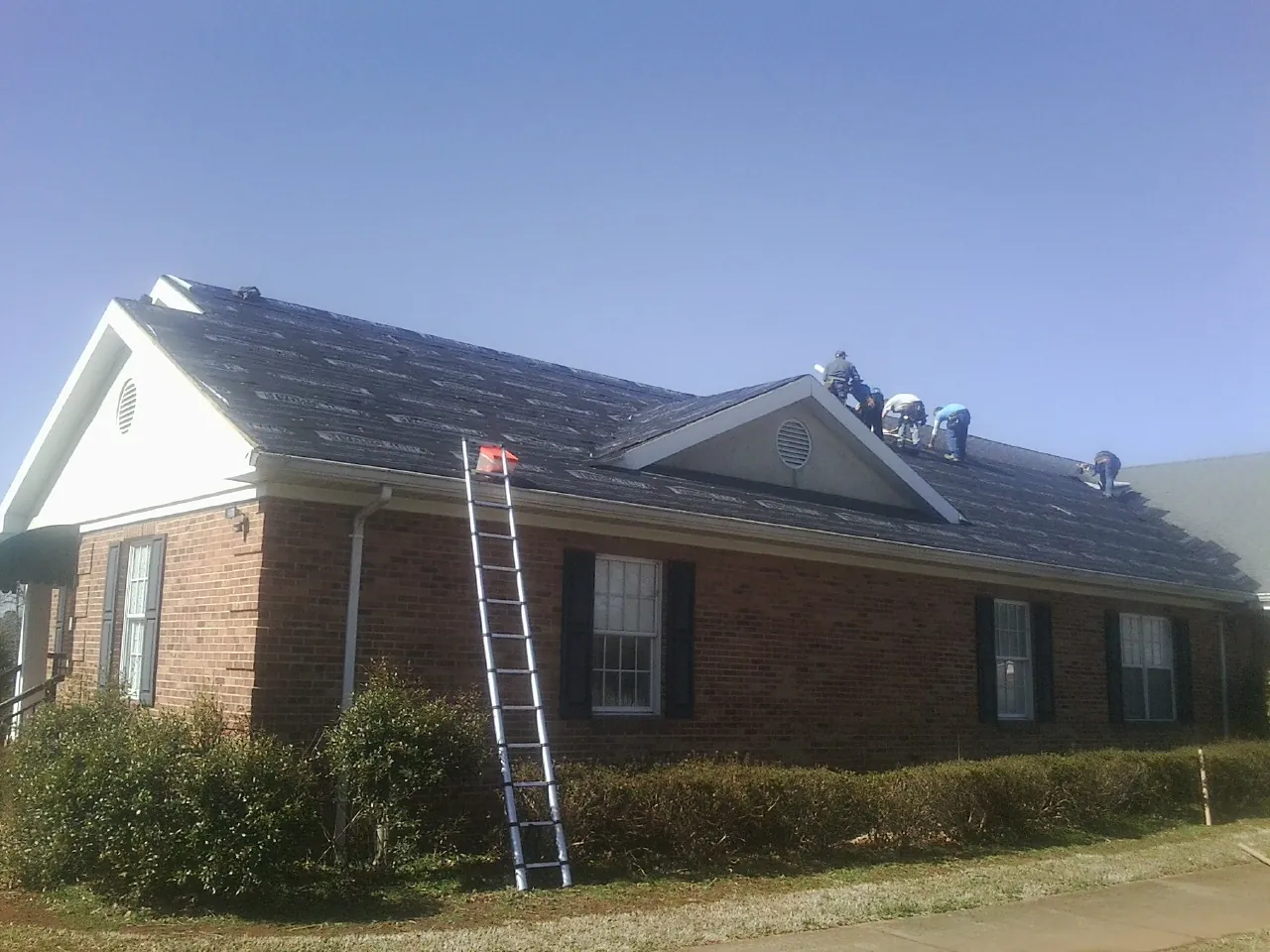 Crew tearing shingles off a brick ranch roof with a ladder set — Emergency Roof Repair work by our crew in Boca Grande