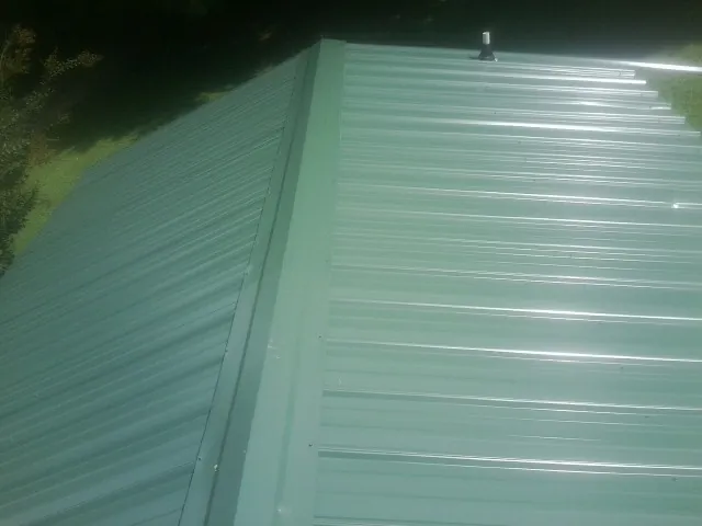 New green metal panels meeting at the ridge of a roof — Flat Roof Repair work by our crew in Boca Grande