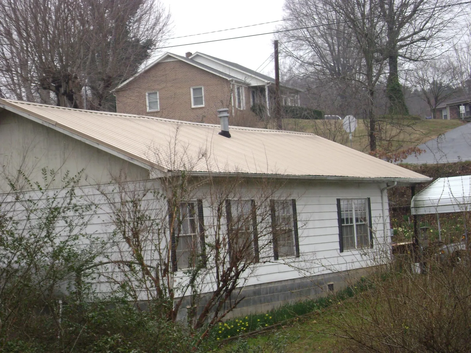 Tan metal roof on a white sided house set into a hillside — Commercial Roofing by Roofing Brothers in Boca Grande